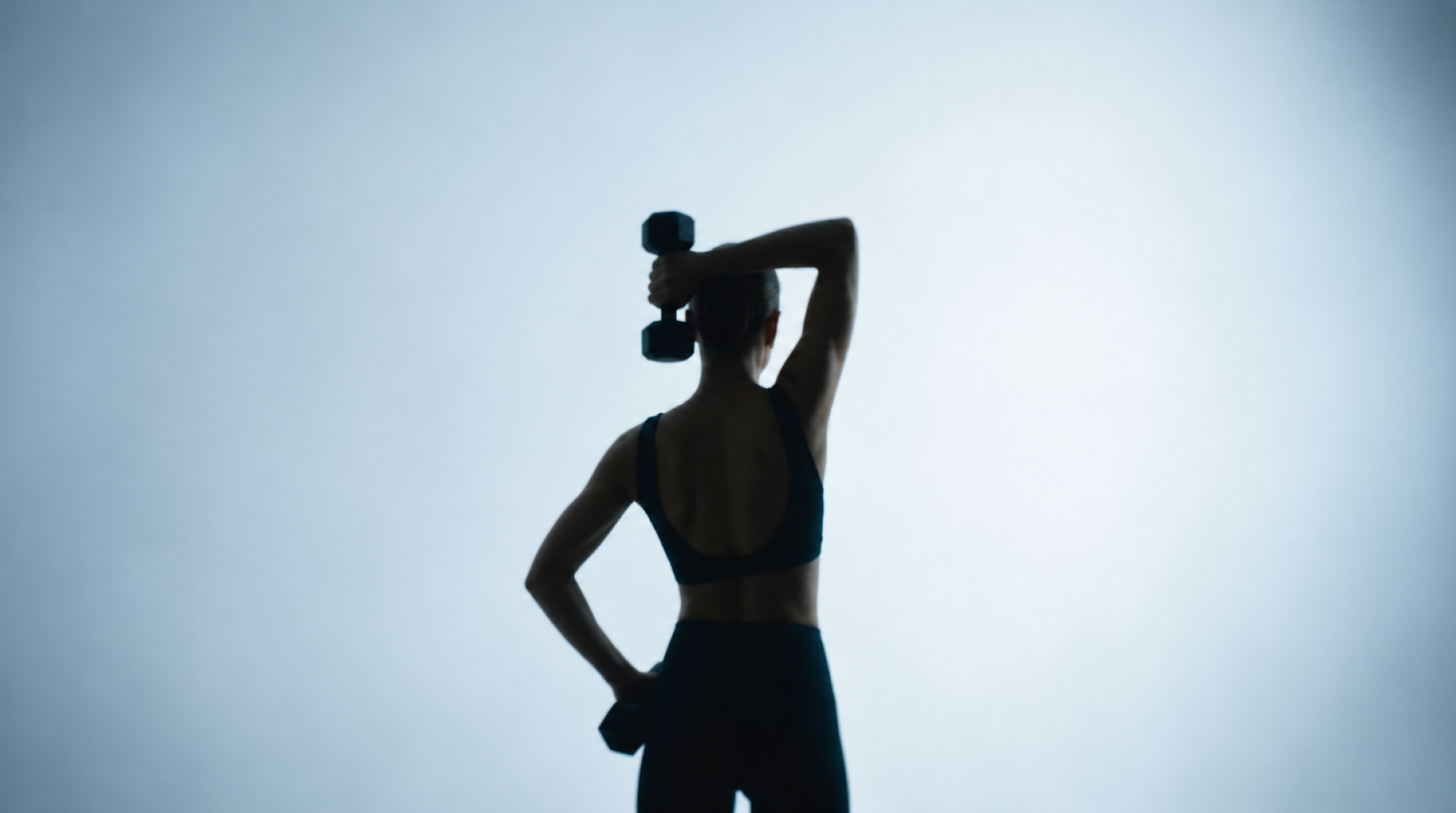 An instructor lifting a hand weight against a softly lit blue studio backdrop.